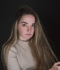 Naklejka premium Portrait of a beautiful, sweet, young girl on a gray background in a beige sweater