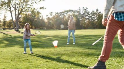 Childcare as it should be. Parents play with daughter in badminton in the park on a sunny day - obrazy, fototapety, plakaty