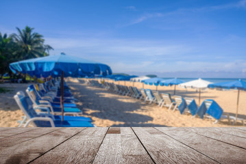 Wooden table top on blurred umbrella and some people relax on the white sand beach and blue sea with blue sky