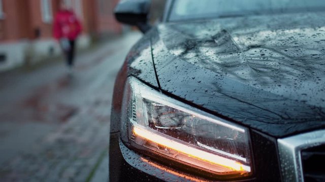 Person out of focus walks towards a parked car and unlocking it in slowmotion on a cloudy and overcast day in Sweden.