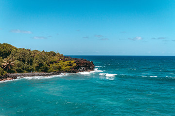 coastline of lava and black sand beach blowhole maui road to hana green jungle palmtrees and blue ocean water and sky