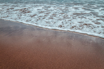 black sand beach at sundown with cloud reflections on wet sand waves washing up
