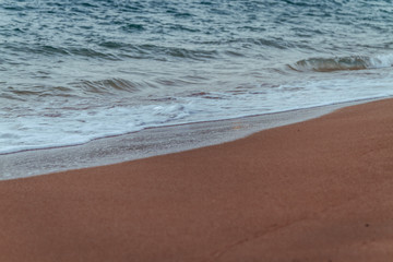 Fototapeta na wymiar black sand beach at sundown with cloud reflections on wet sand waves blue water 