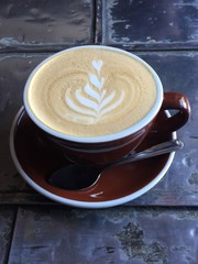Latte espresso drink in mug on saucer with spoon on metal tin tile table
