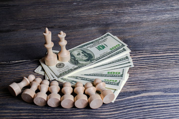 white chess pieces stand on a wad of American money in front of fallen pawns