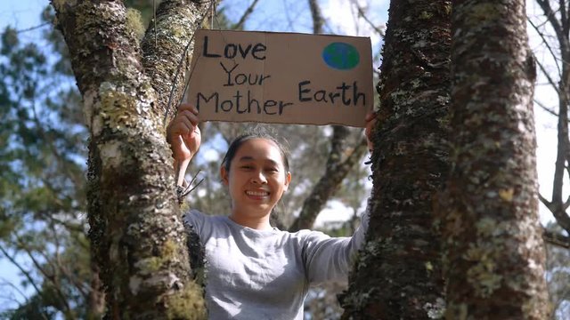 Asian young woman holding "Love your Mother Earth" Poster on a demonstration due to climate change by plastic pollution. Female standing in the park with a sign to save the world.