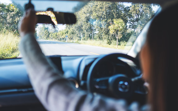 A Woman Adjusting A Rear View Mirror While Driving Car