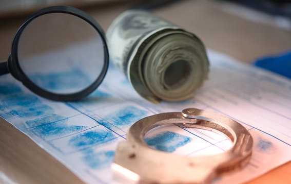Police handcuffs and Magnifying glass with a lot of dollar rolls on police fingerprint crime page file. Economic Crime or illegal possession of money.