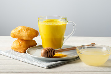 Golden milk with turmeric and honey, a traditional Indian drink on a white wooden background