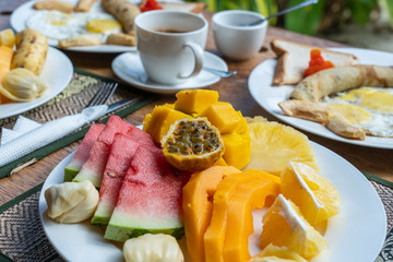 Tropical breakfast of fruit, coffee and scrambled eggs and banana pancake for two on the beach near sea