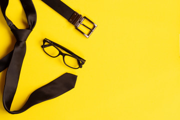 Top view of glasses, belt and tie over yellow background. business men or entrepreneur guy concept.