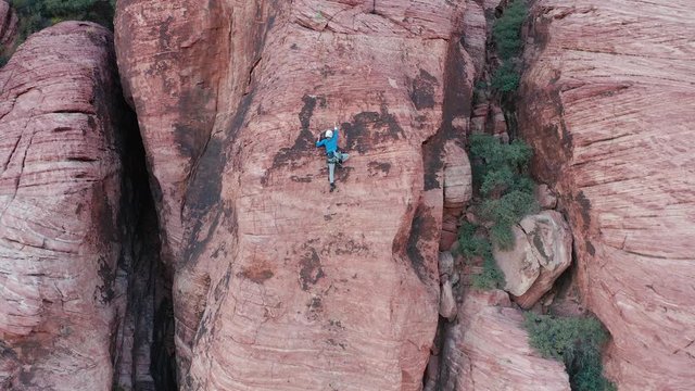 Aerial moving shot of athletic female rock climbing up a steep sandstone wall