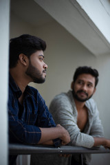 Two young tall, dark and handsome Indian Bengali men in western jackets and shirt spending time together standing on balcony in white background. Indian lifestyle.