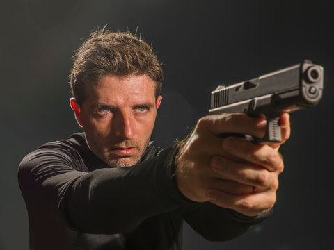 attractive hitman or special agent man holding gun pointing the weapon isolated on dark background in secret service Hollywood style movie