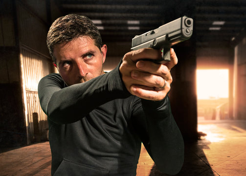 action portrait of serious and attractive hitman or special agent man holding gun pointing the weapon at cinematic edgy background in secret service movie Hollywood style