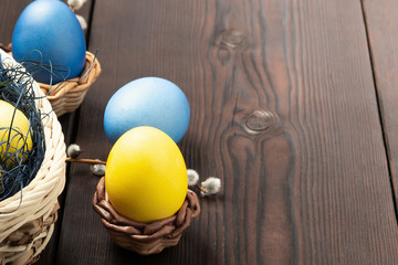 Easter composition - several colored eggs in a basket and on a dark wooden table with willow twigs, place for text, copy space