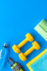 Fitness background - dumbbells, jump rope, sport carpet, water bottle - on blue top-down frame copy...