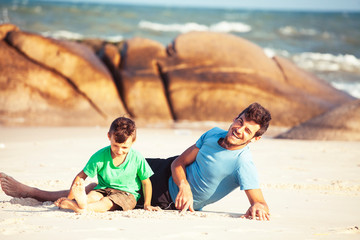 Fototapeta na wymiar happy family on beach playing, father with son walking sea coast, rocks behind smiling taking vacation
