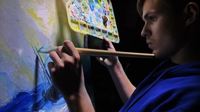 Artist copyist paint seascape with ship in ocean. Craftsman decorator draw as boat sail on blue sea with acrylic oil color. Draw finger, brush, knife palette. In hand of cellphone tablet computer pc.