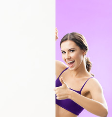 Fitness, sport, training and healthy lifestyle concept - young woman in fitness wear showing blank signboard or copyspace, on rose background