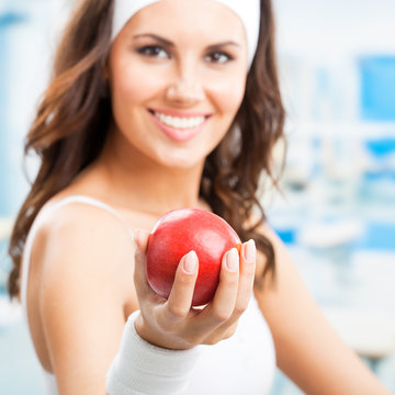 Fitness, sport, training and healthy lifestyle concept - woman giving red apple, at fitness center or gym, selective focus on hand.
