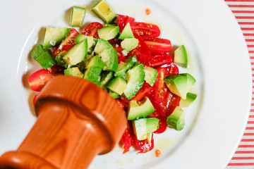 Stockholm, Sweden A tomato and avocado salad on a white plate with olive oil and a pepper mill.