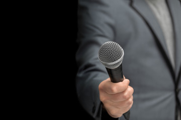 Interviewer or reporter with a microphone in hand, on an insulated black background. Grey jacket