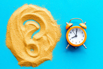 Deadline concept. Clock near question mark on sand on blue background top-down