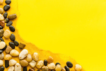 Sea rest, summer vacation concept. Stones and sand on yellow background top-down frame copy space