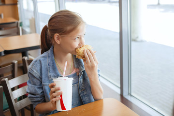 Girls Teenagers at a table in a cafe eat sandwiches and drink soda.