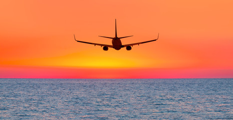 Passenger plane flying over the sea, beautiful sunset 