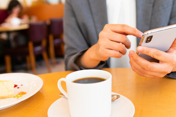 コーヒー片手にスマホを操作する女性