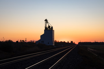 Fototapeta na wymiar Grain Elevator Silhouetted Against Golden Prairie Sunrise