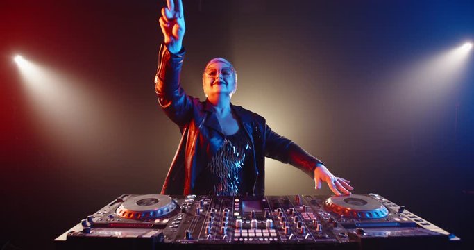 Funny caucasian grandma in authentic outfit and makeup working as a cool dj in a nightclub, dancing and cheering at turntables 4k footage