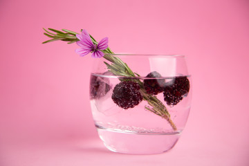 gin and tonic with blackberries, a sprig of rosemary and a flower of ornament