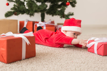 Cute baby girl wearing santa claus suit crawling on floor over Christmas tree. Holiday season.