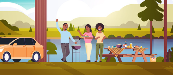 friends preparing hot dogs on grill african american man and women having fun picnic barbecue party concept park or river bank landscape background flat full length horizontal vector illustration