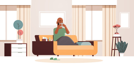 sick man blowing nose with handkerchief unhealthy african american guy cleaning snotty nose having flu sneeze sitting on sofa illness concept modern living room interior full length horizontal vector