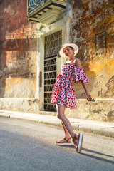 Young woman in a colored dress and white hat on a street