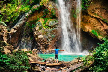 A man standing in front of big waterfall in the jungle. Travel Indonesia. Hidden beauty of the island. Man standing at the bottom of the fall shows the scale of the waterfall