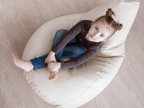 5 years girl child with big grey eyes in pink pajamas lay on blue ottoman and looks up with smile. day of sleep. Happiness, leisure and lifestyle in childhood.