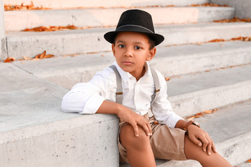 Cute fashionable African-American boy sitting on stairs outdoors