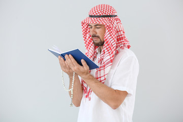 Muslim man with Koran and beads on light background