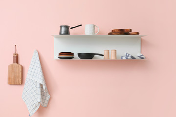 Shelf with utensils hanging on color wall