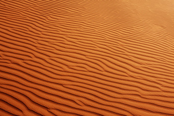Fototapeta na wymiar Wavy sandy texture on the dunes in the desert. View from above