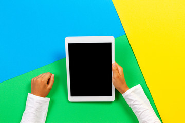 Hands holding tablet computer on yellow, blue and green background. Top view