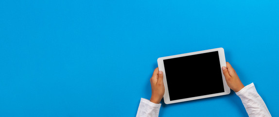 Kid hand holding white tablet computer on light blue background