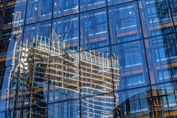 Modern building under construction at a bright sunny day on the blue sky background. Reflection of tower cranes on windows mirror. Low angle view