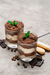 Classic tiramisu dessert in a glass cup, savoiardi cookies and pieces of chocolate on concrete background