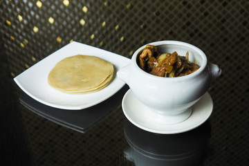 On the dark table is a pot of pork cooked in curry sauce and a plate with Chinese cakes.